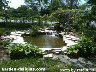 Large backyard pond with shale stone around edge with barrel waterfall at one end with vegetation, backyard garden pond designs, backyard pond ideas.