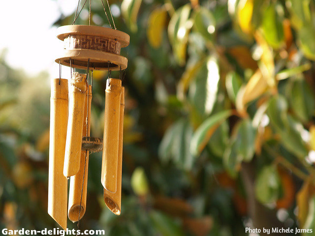  Bamboo wind chimes with five bells and a wooden striker with a ring top and carved decorations in the wood hanging topper hung in the tree with sunshine on one side, bamboo wind chime crafts, hanging windchimes, whimsical windchimes, wooden windchimes, breezy with music windchimes, Hawaiian bamboo chimes, sensory garden ideas, windchimes sun Dreamcatcher, garden windchimes, creating a natural look and appearance with beautiful wind music created by a soft breeze.