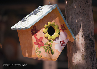 Small cute birdhouse with flowers on front and blue roof hanging in tree, unique birdhouses, birdhouse decorating.