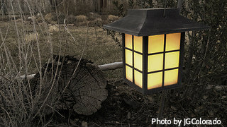 Black metal lantern on post in garden beside tree stump, garden hanging lanterns, outdoor decorative lanterns.