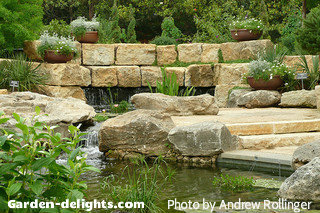 Small yard waterfall and stream with decorative rocks on both sides with potted flowers, backyard ponds, garden ponds.