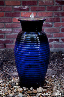 Ceramic vase/urn water fountain with decorative colored (black, blue) coil rings on decorative rock bed, ceramic garden water fountains.
