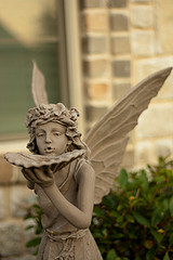 Stone fairy statue with wings holding a seashell up to her face, fantasy water features, solar powered fairy water fountains.