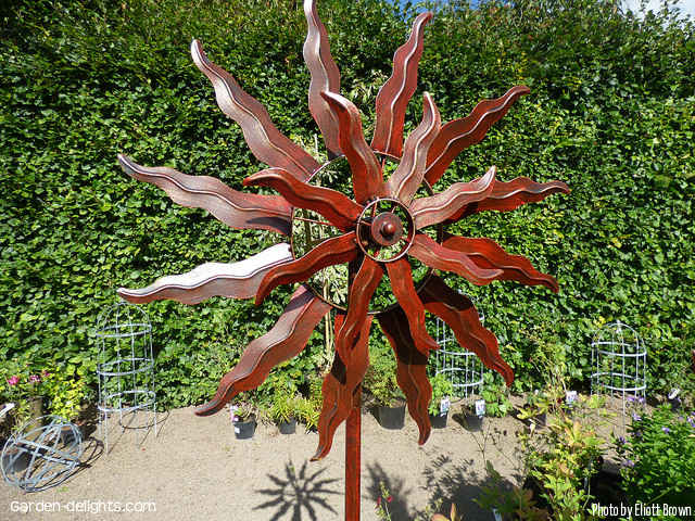  Large red metal kinetic wind spinner that looks like the sun mounted on the post in secret garden, kinetic spinners, garden wind decorations, secret garden accents.