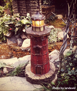 Miniature red lighthouse with light beacon turned on beside garden pond, miniature garden lighthouses, ornamental lawn lighthouses.