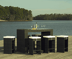 Outdoor Bar Furniture, Wicker bar set with five stools and white cushions with martini glasses on top in front of Lake.