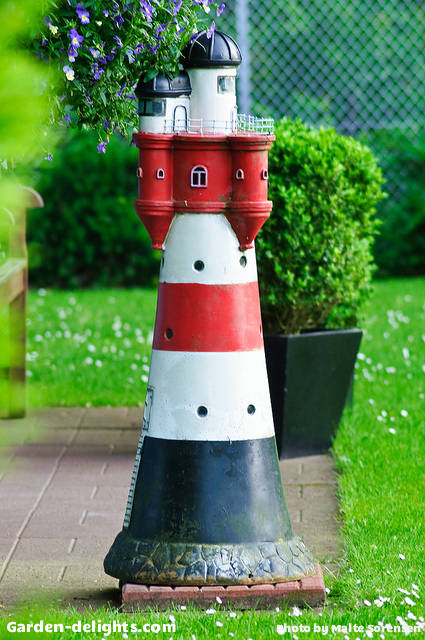  Small lighthouse on brick patio with black white and red striped with Castle top design and small windows, solar lighthouse with rotating beacon, lighthouse lawn ornament, lawn lighthouse with rotating solar beacon