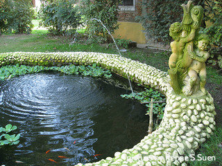 Large round pond with marginal flowers and kio fish surrounded with small boulders and garden statue, garden pond directory, outdoor pond tips