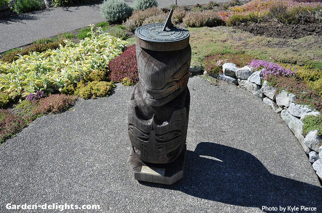  Ancient carved wooden sundial pedestal with green metal sundial mounted on top in garden walkway, antique pedestals for sale, stone, cast-iron, Rome sundial pedestal base, sundial stands, mounting for sundials.