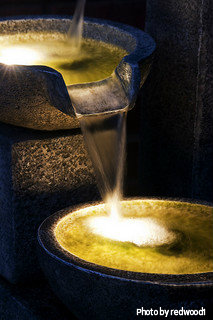 Multilevel small stone lighted water fountain with yellow, orange decorative lighting pouring water from spout into basin, lighted corner fountains, illuminated water feature.