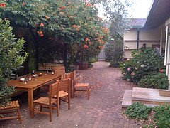  Cedar Wood Outdoor Furniture, wood table and six chairs on brick patio with trees overhanging.