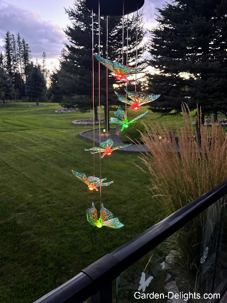 Solar powered dragonfly wind chimes mobile hanging on deck with LED multicolor lights glowing in red, green, yellow, explore solar LED dragonfly chimes, garden solar chimes.